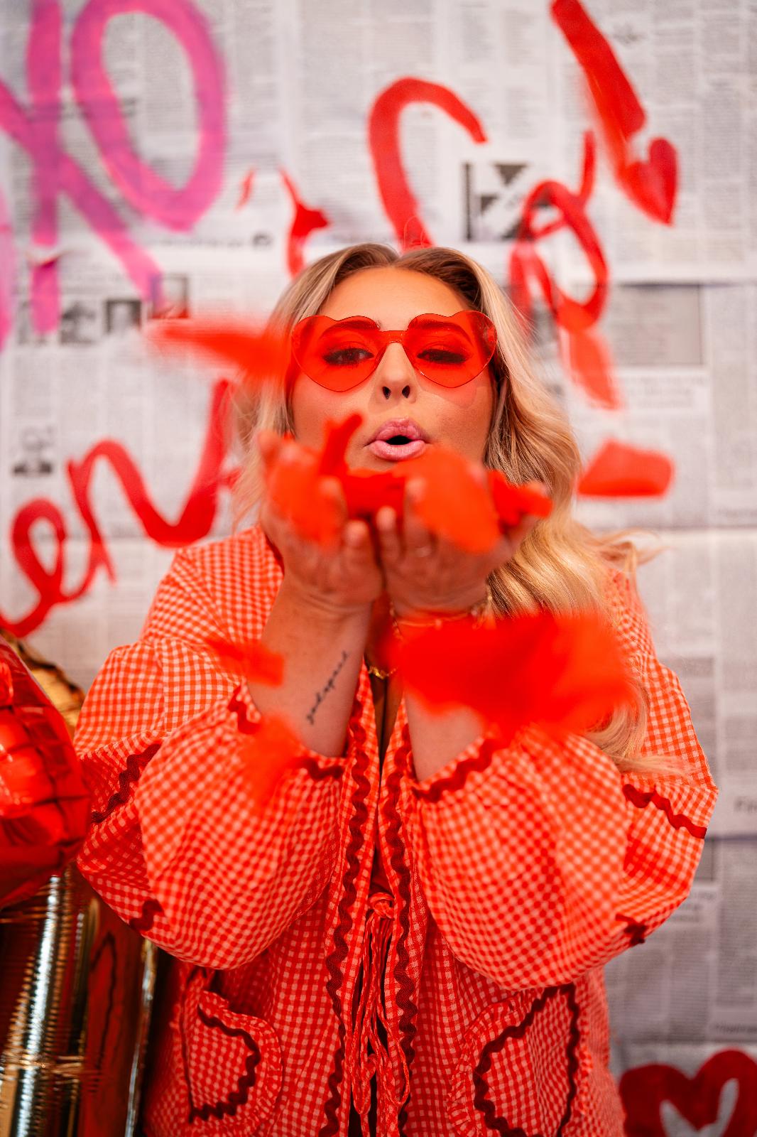 blonde woman blowing heart confetti into the camera